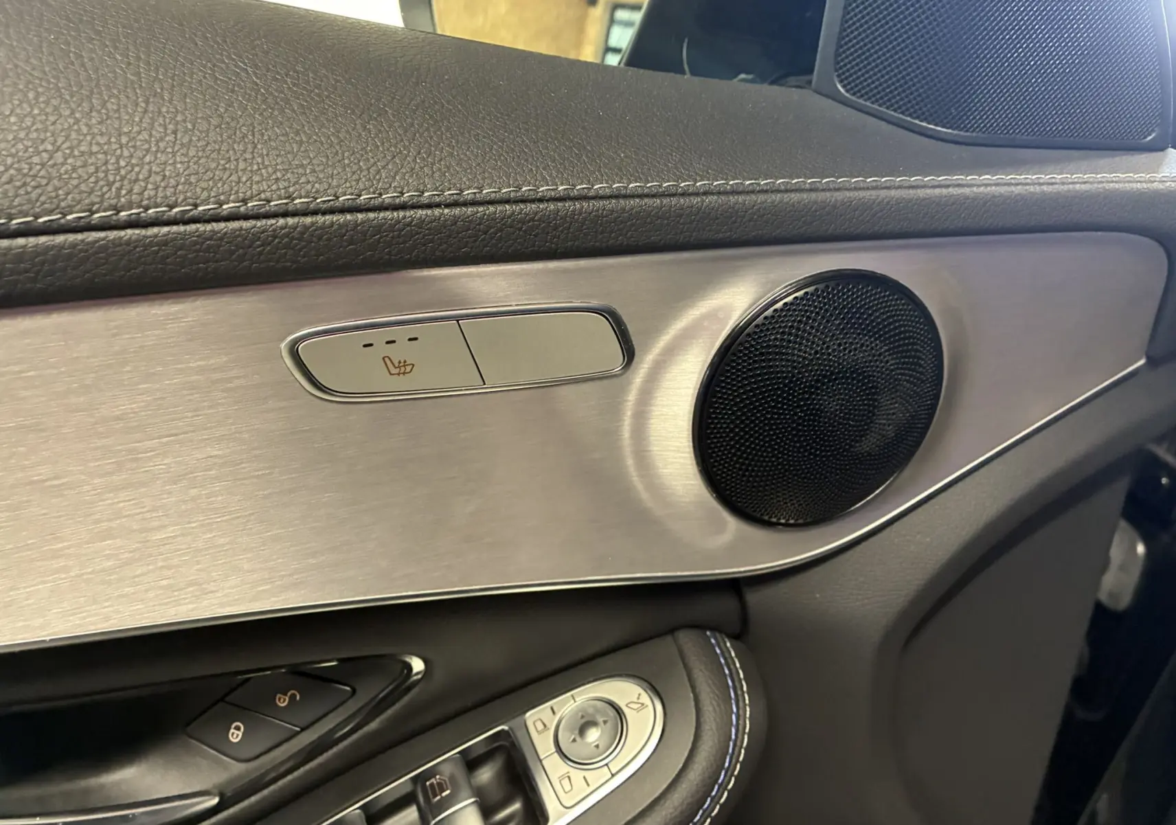 Détail intérieur côté gauche de la porte d'une Mercedes Classe C Break 220D AMG Line 2021, avec bouton siège chauffant et haut-parleur.