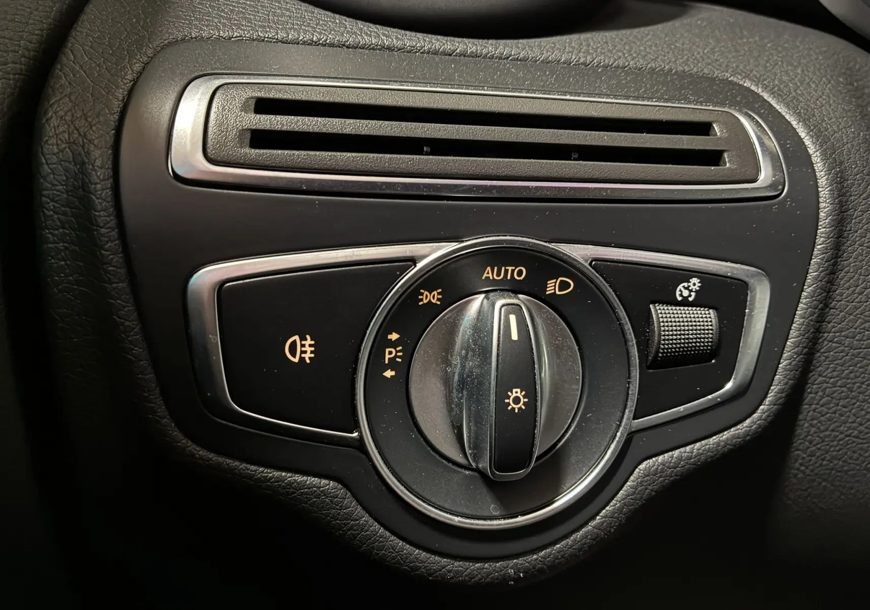 Gros plan sur la commande des feux avec molette et réglage d’intensité dans l’habitacle noir d’une Mercedes Classe C Break 220D AMG Line.
