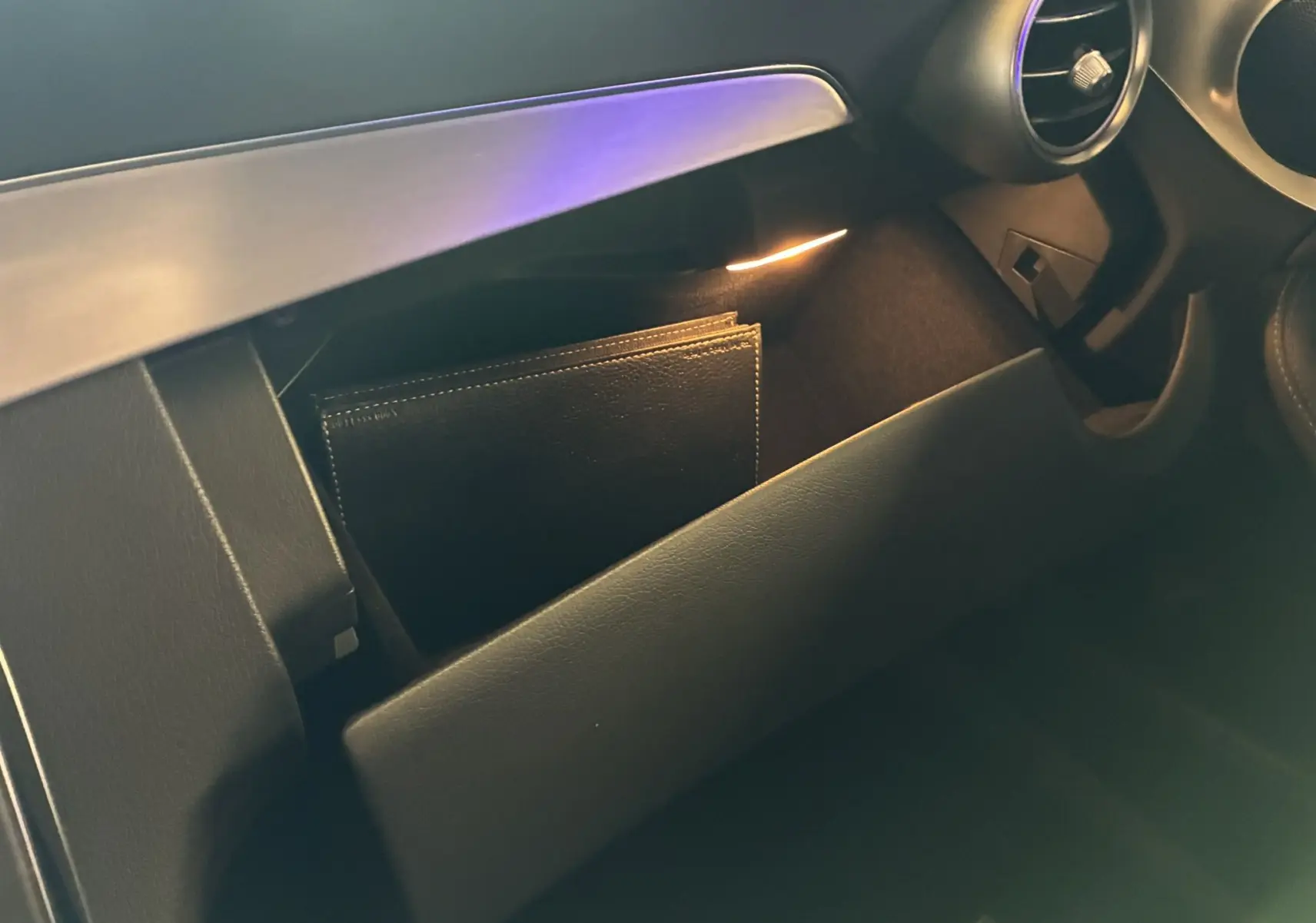 Gros plan sur la boîte à gants ouverte du Mercedes Classe C Break 220D AMG Line, éclairage intérieur doux visible.