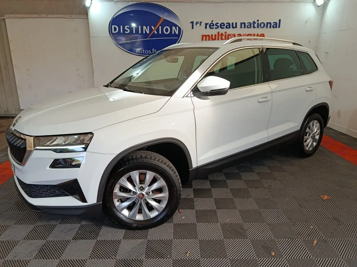 Vue 3/4 avant droite d’un Skoda Karoq blanc 2024, avec jantes alliage et rétroviseurs blancs, en intérieur showroom.