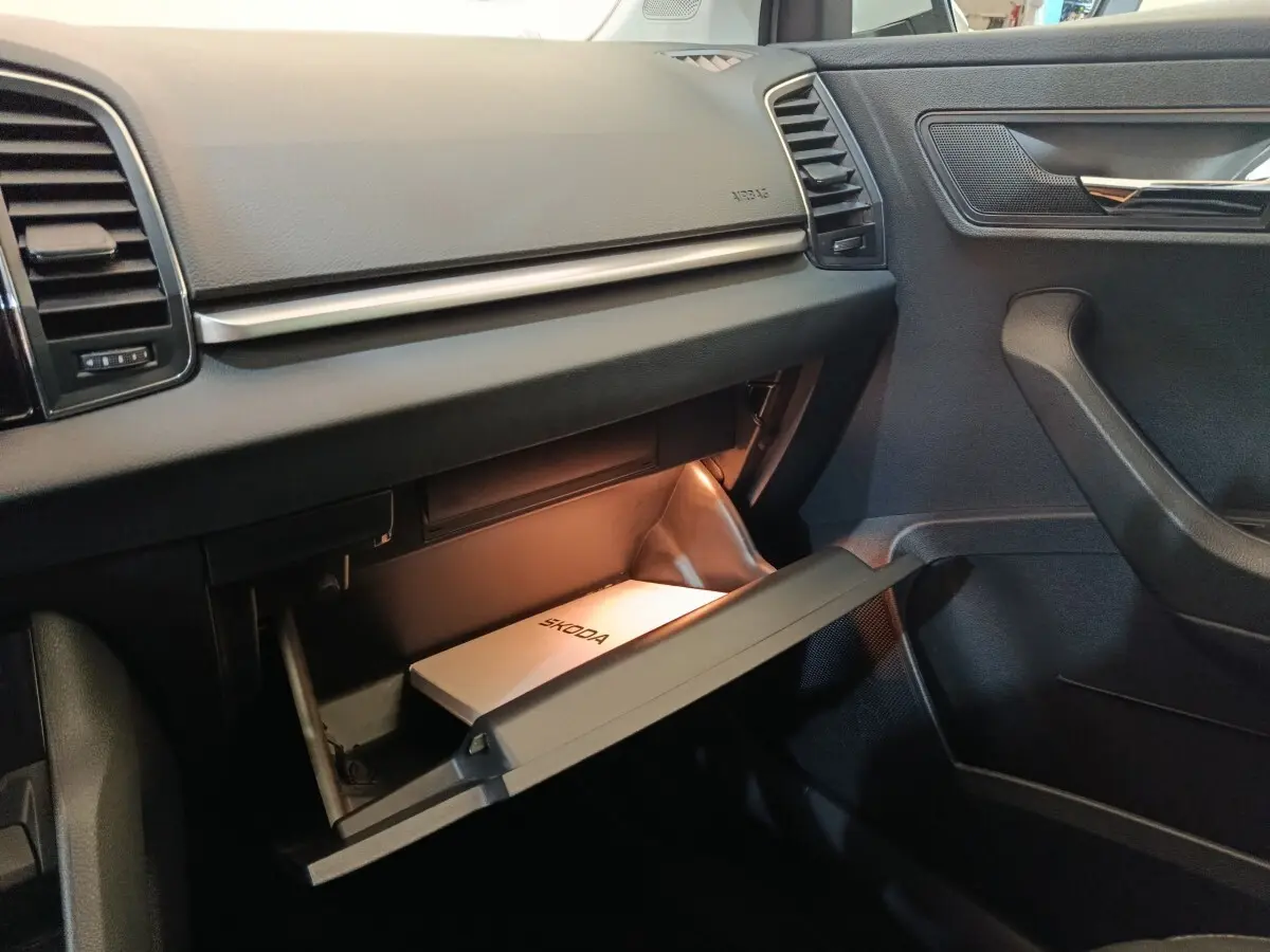 Intérieur noir de la Skoda Karoq 2024, vue côté passager avec boîte à gants ouverte et manuel Skoda visible.