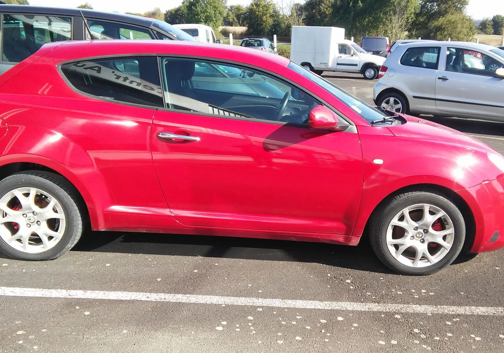 Profil côté gauche de l'Alfa Romeo MiTo Distinctive rouge de 2010, compacte et sportive, garée en extérieur sur un parking.