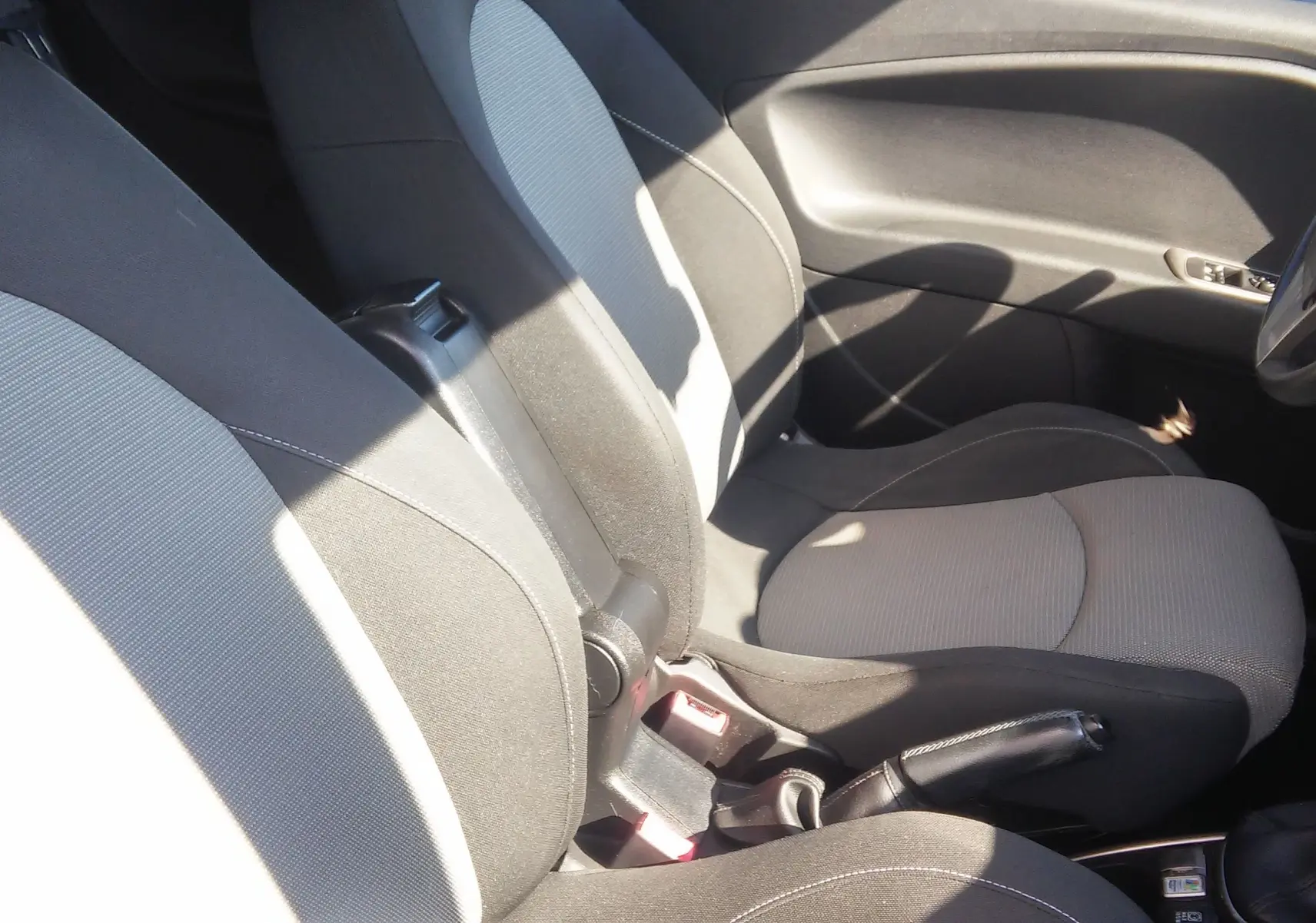 Vue intérieure côté conducteur de l'Alfa Romeo MiTo 2010 avec sièges tissu noir et gris, frein à main et volant visibles.