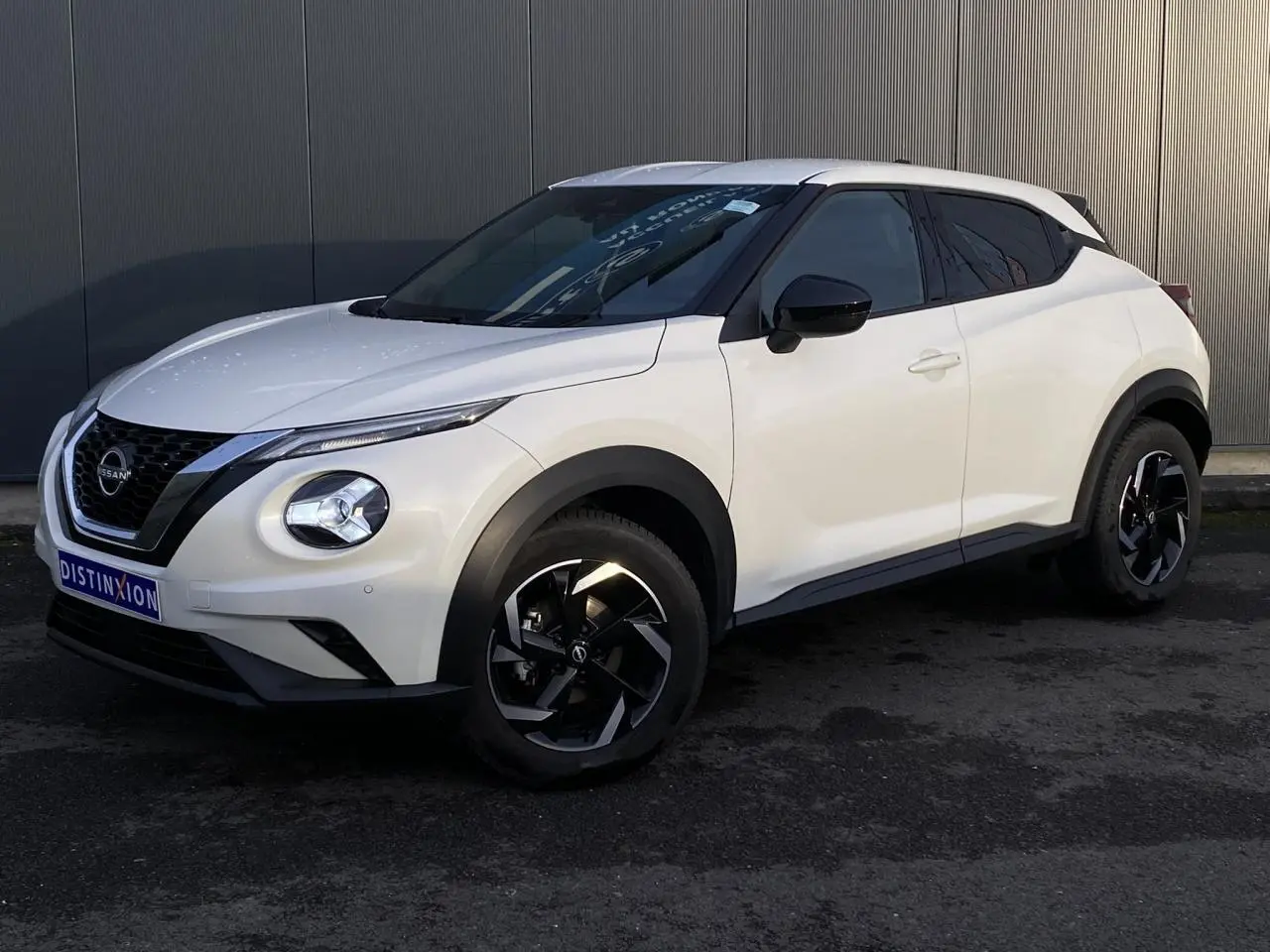 Nissan Juke blanc perle en vue 3/4 avant droit, avec jantes alliage noires et toit blanc contrasté.