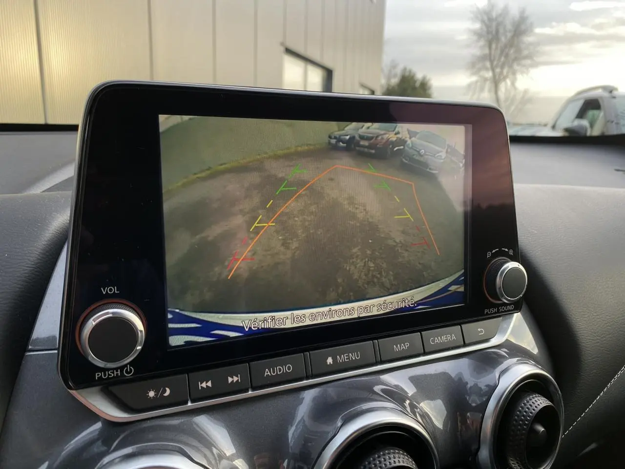 Écran tactile du Nissan Juke blanc perle 2024 montrant la caméra de recul avec lignes d’aide au stationnement.