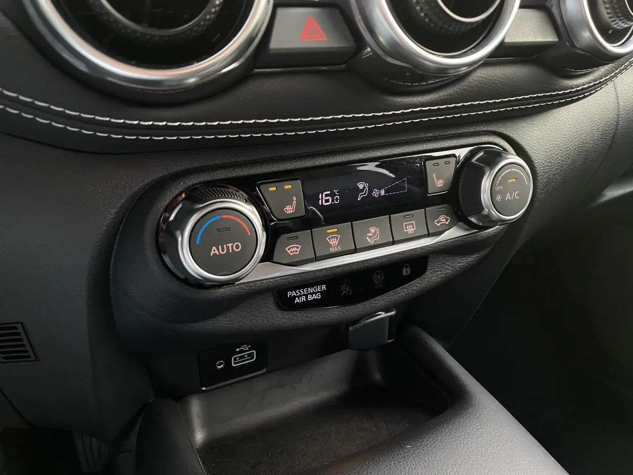 Vue rapprochée de la console centrale noire du Nissan Juke 2024, montrant les commandes de climatisation et sièges chauffants.
