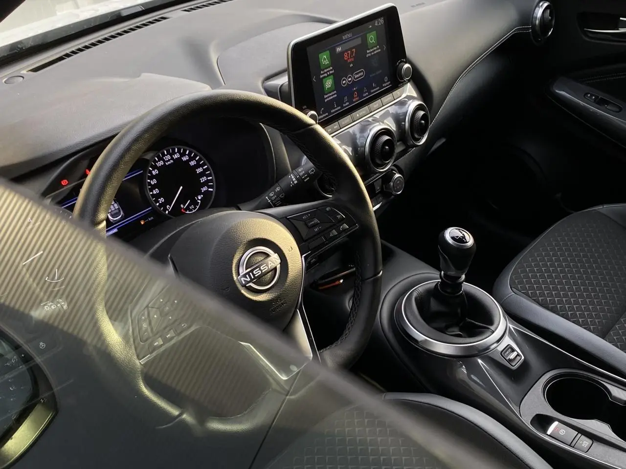 Vue intérieure côté conducteur du Nissan Juke DIG-T 114 N-Connecta 2024, volant cuir, écran tactile et levier de vitesse manuel.