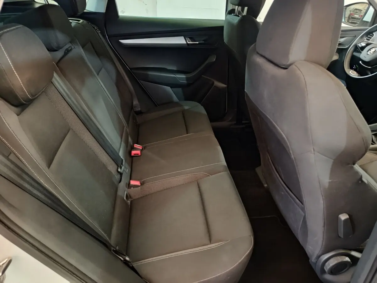 Vue intérieure côté gauche montrant la banquette arrière noire du Skoda Karoq 2024 avec sièges tissu et ceintures visibles.