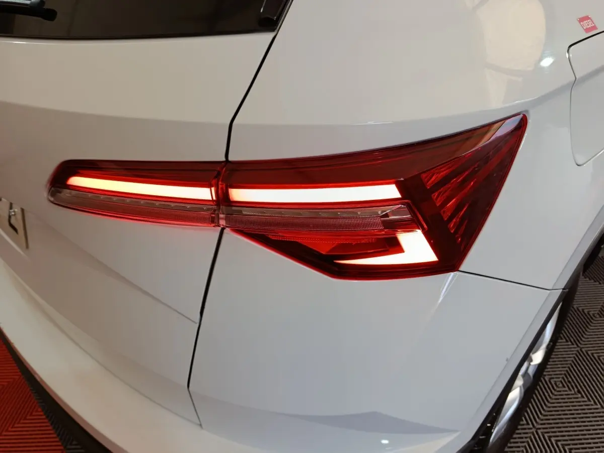 Feu arrière droit allumé sur SKODA KAROQ blanc 2024, vue rapprochée du coffre et porte carburant.