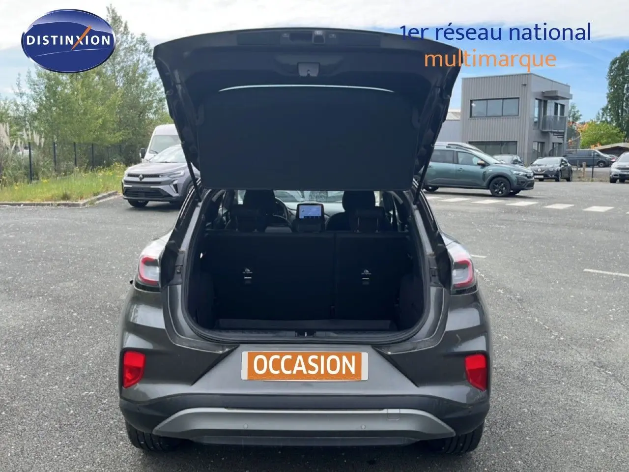 Vue arrière d'un Ford Puma gris 2021 avec coffre ouvert, mettant en valeur l'espace de chargement et les feux arrière.