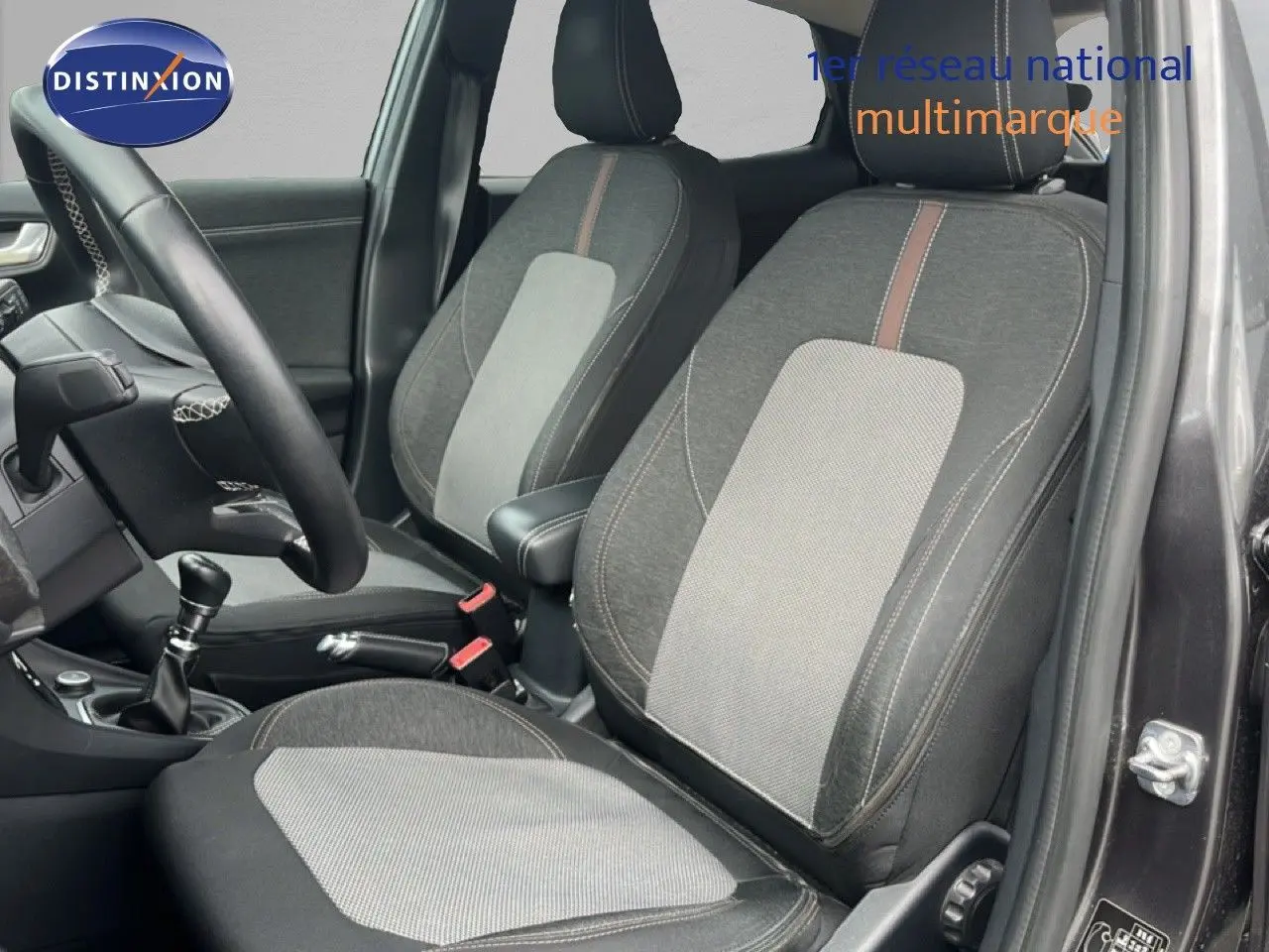 Vue intérieure côté conducteur du Ford Puma gris 2021, montrant les sièges tissu bicolore et la boîte manuelle.