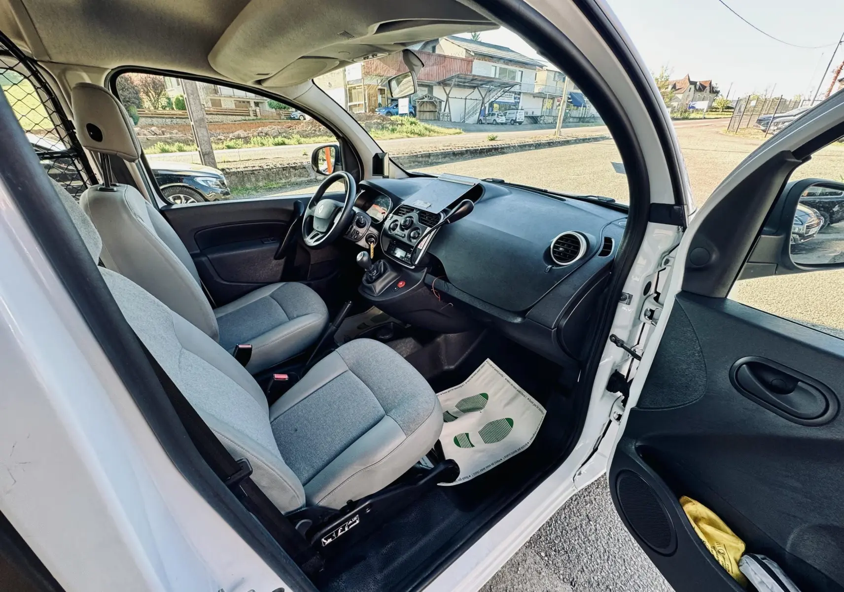 Vue intérieure côté conducteur du Renault Kangoo blanc de 2021, montrant les sièges gris et le tableau de bord noir.