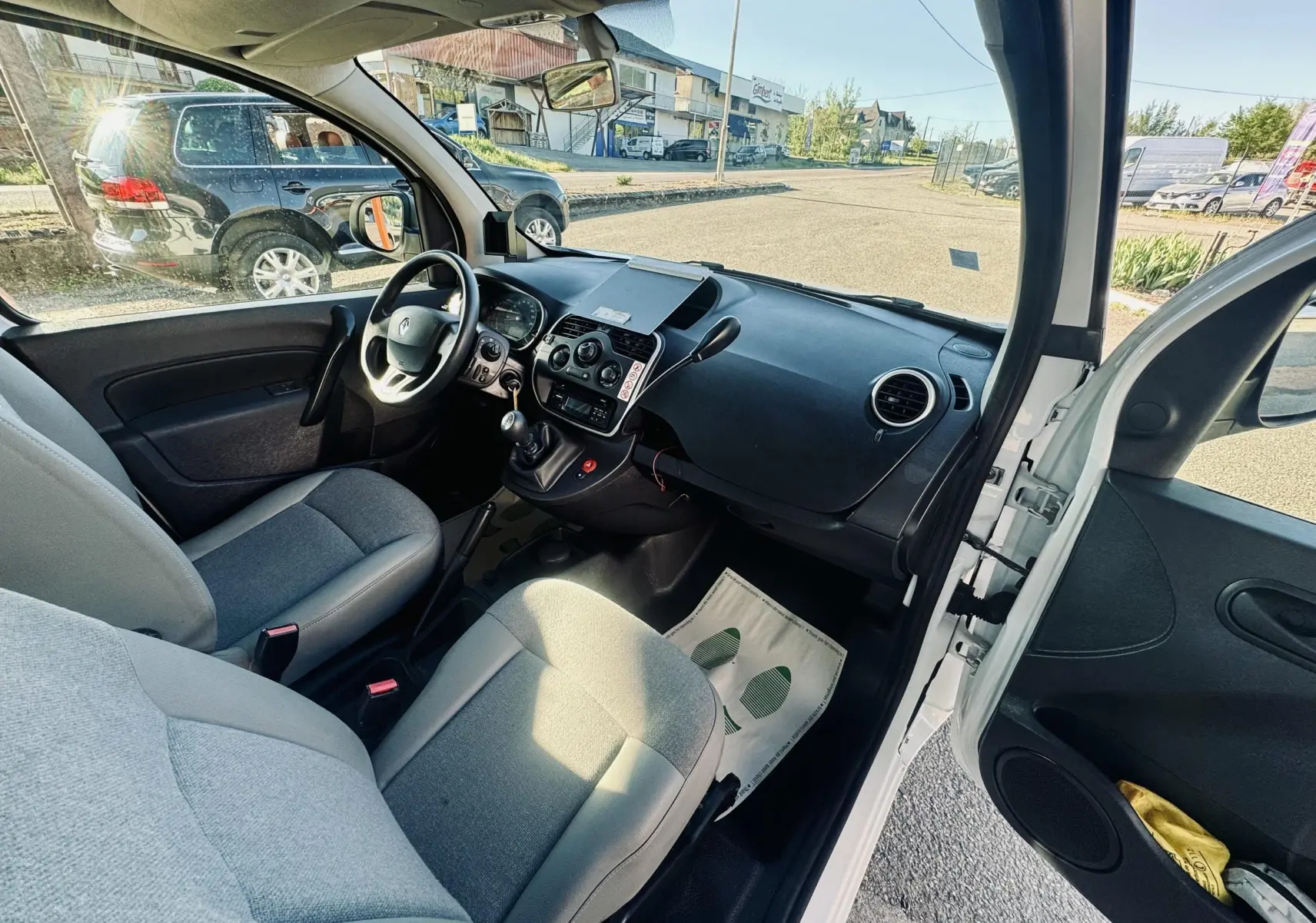 Vue intérieure côté conducteur du Renault Kangoo blanc 2021, montrant le tableau de bord et les sièges en tissu gris.