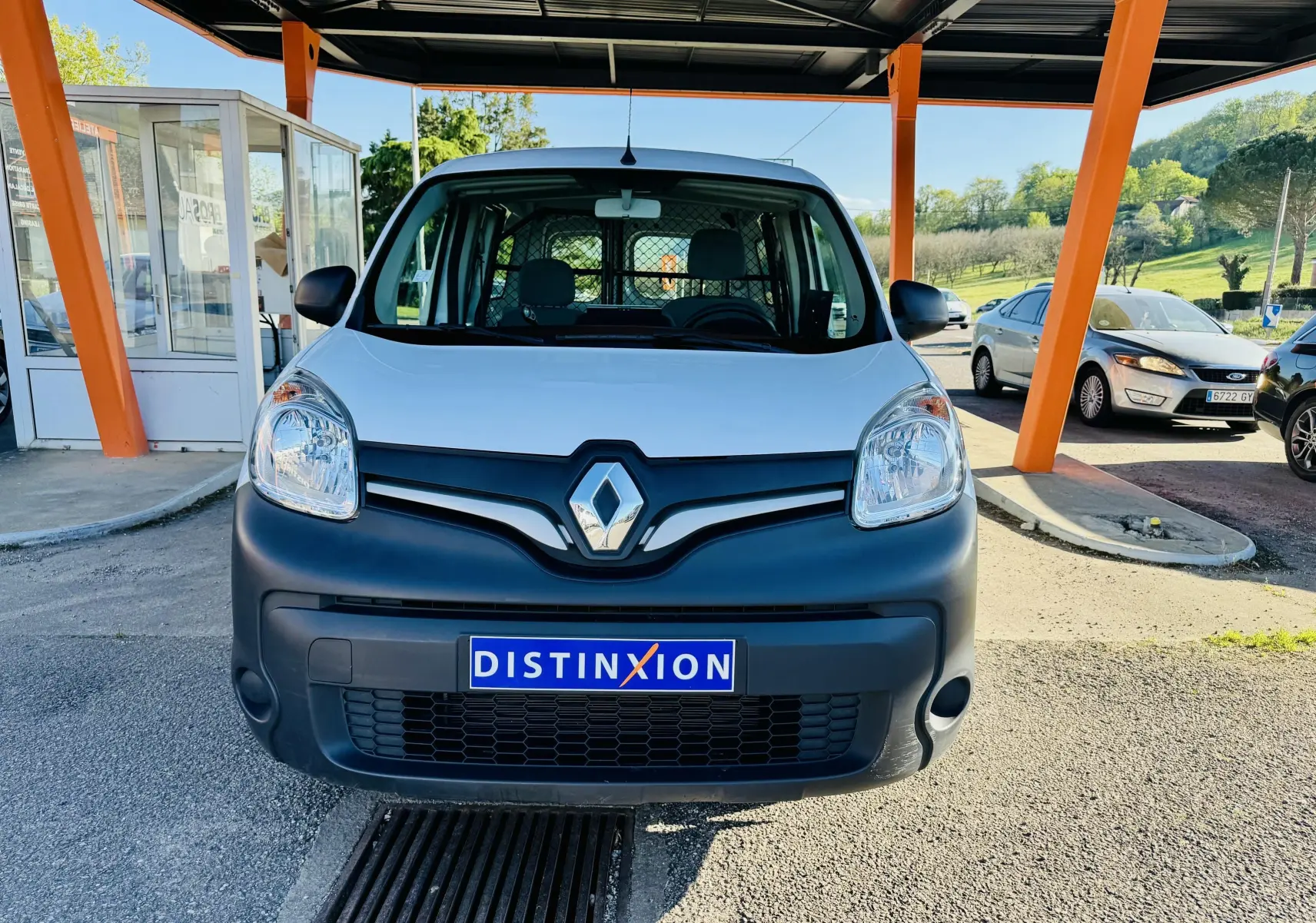 Vue avant d’un Renault Kangoo Maxi blanc avec pare-chocs noir et calandre marquée du logo Renault sous un abri orange.