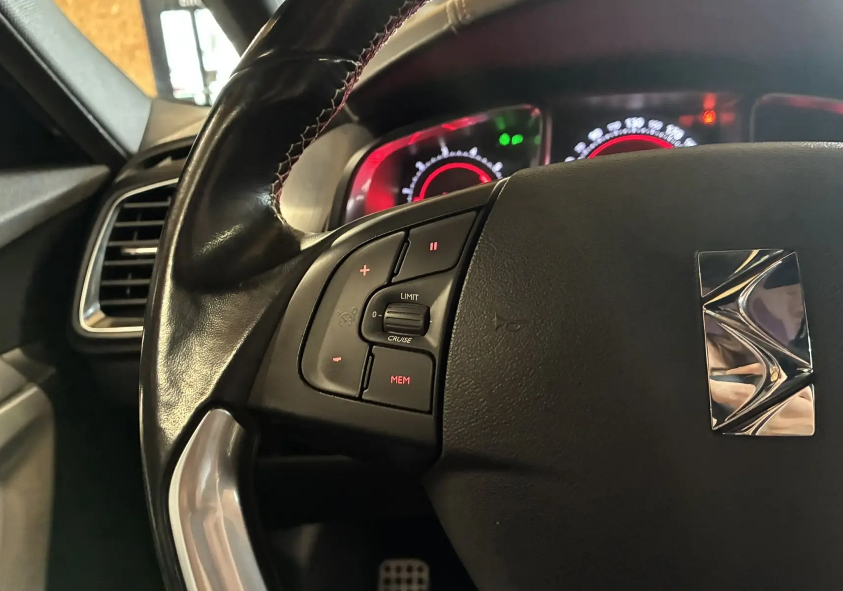 Gros plan sur le volant noir de la DS5 2018 avec commandes intégrées et tableau de bord éclairé en rouge en arrière-plan.