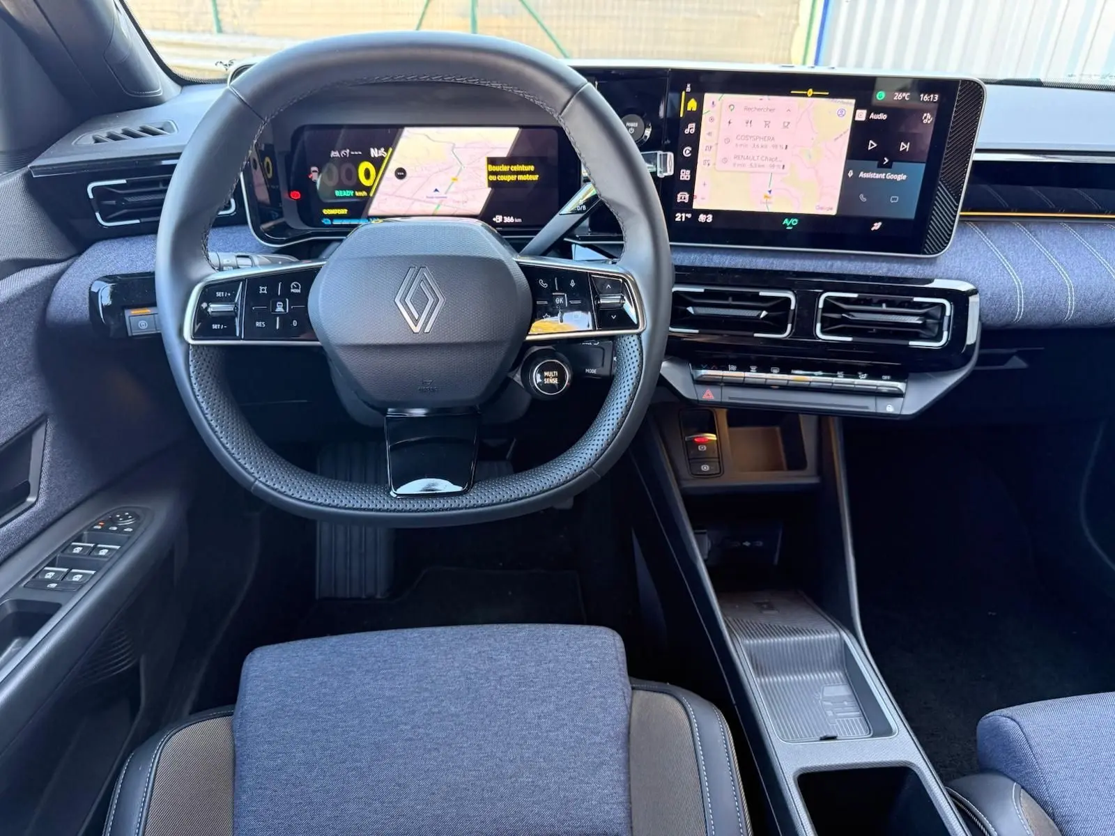 Vue intérieure frontale du tableau de bord et volant Renault R5 E-TECH 100% électrique avec écran tactile et sellerie textile bleue.