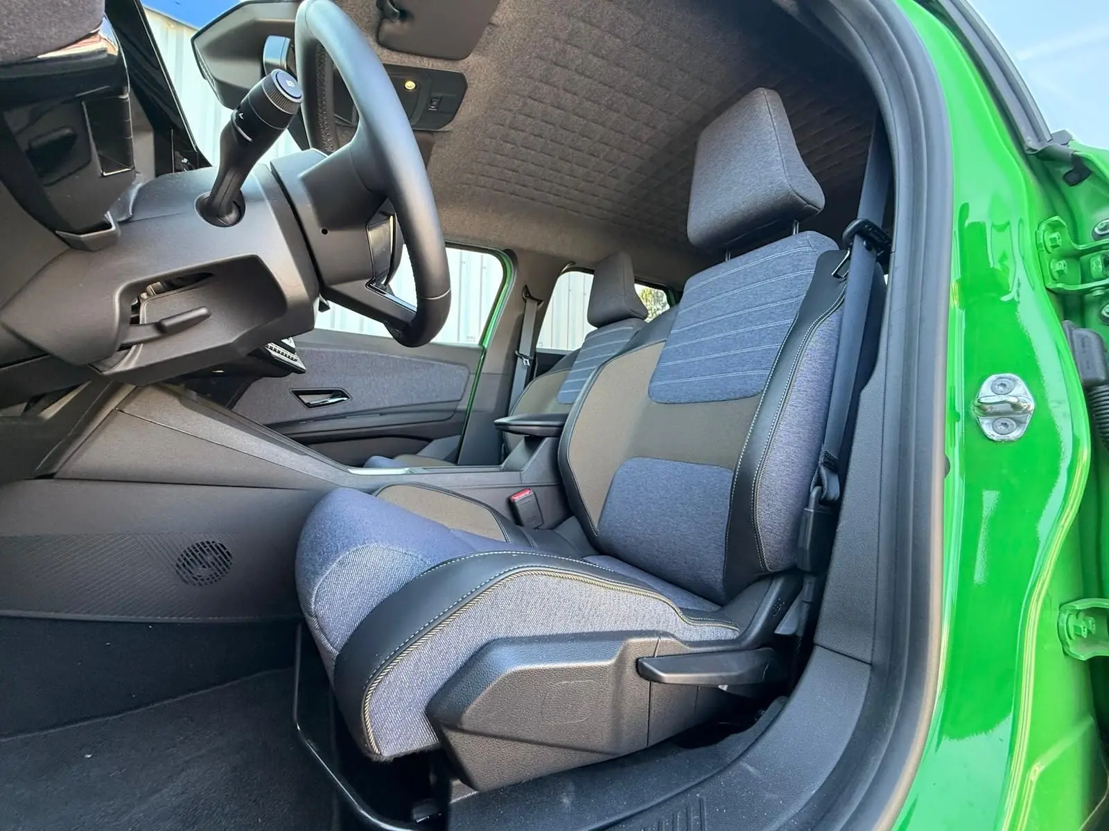 Vue intérieure côté conducteur de la Renault R5 E-Tech 2024 avec sellerie textile bleu jean et portière verte Pop ouverte.