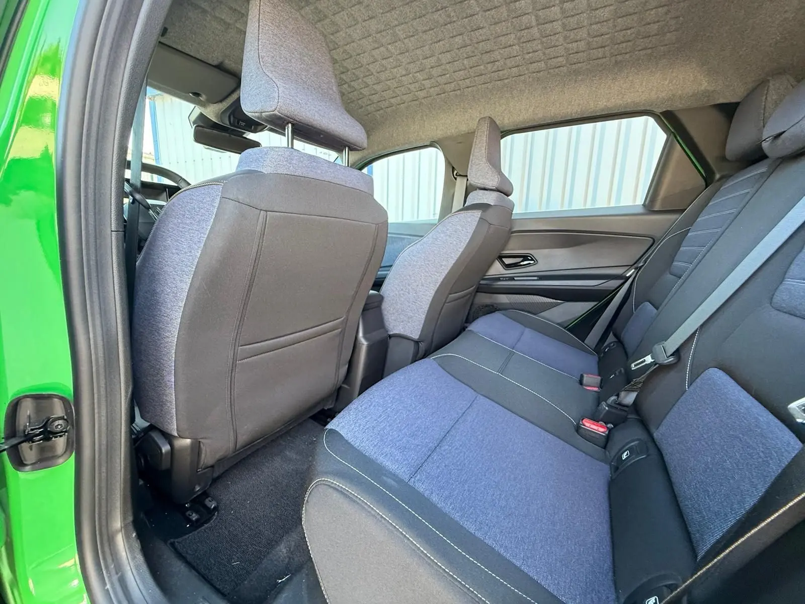 Vue intérieure arrière côté gauche de la Renault R5 E-TECH 100% électrique, sellerie textile bleu et noir, porte verte ouverte.