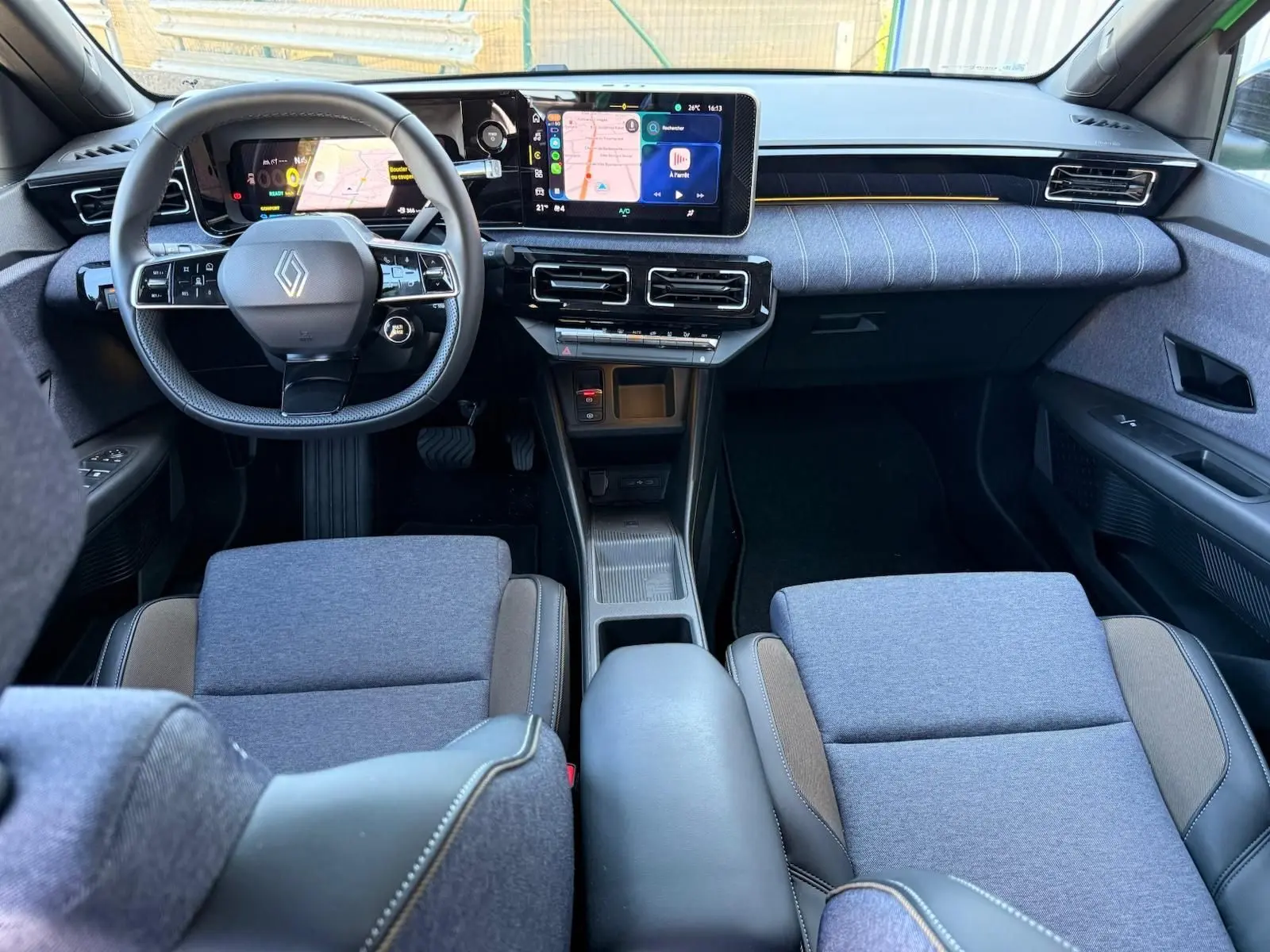 Vue intérieure avant de la Renault R5 E-TECH 100% électrique, avec sellerie textile gris jean et tableau de bord moderne.