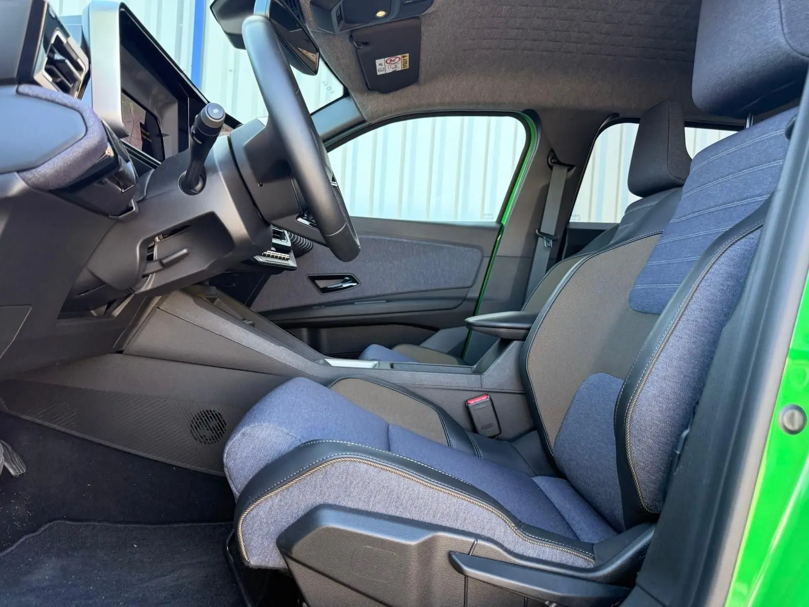 Vue intérieure côté conducteur de la Renault R5 E-TECH 100% électrique 2024, sellerie textile recyclé bleu et noir, porte verte.