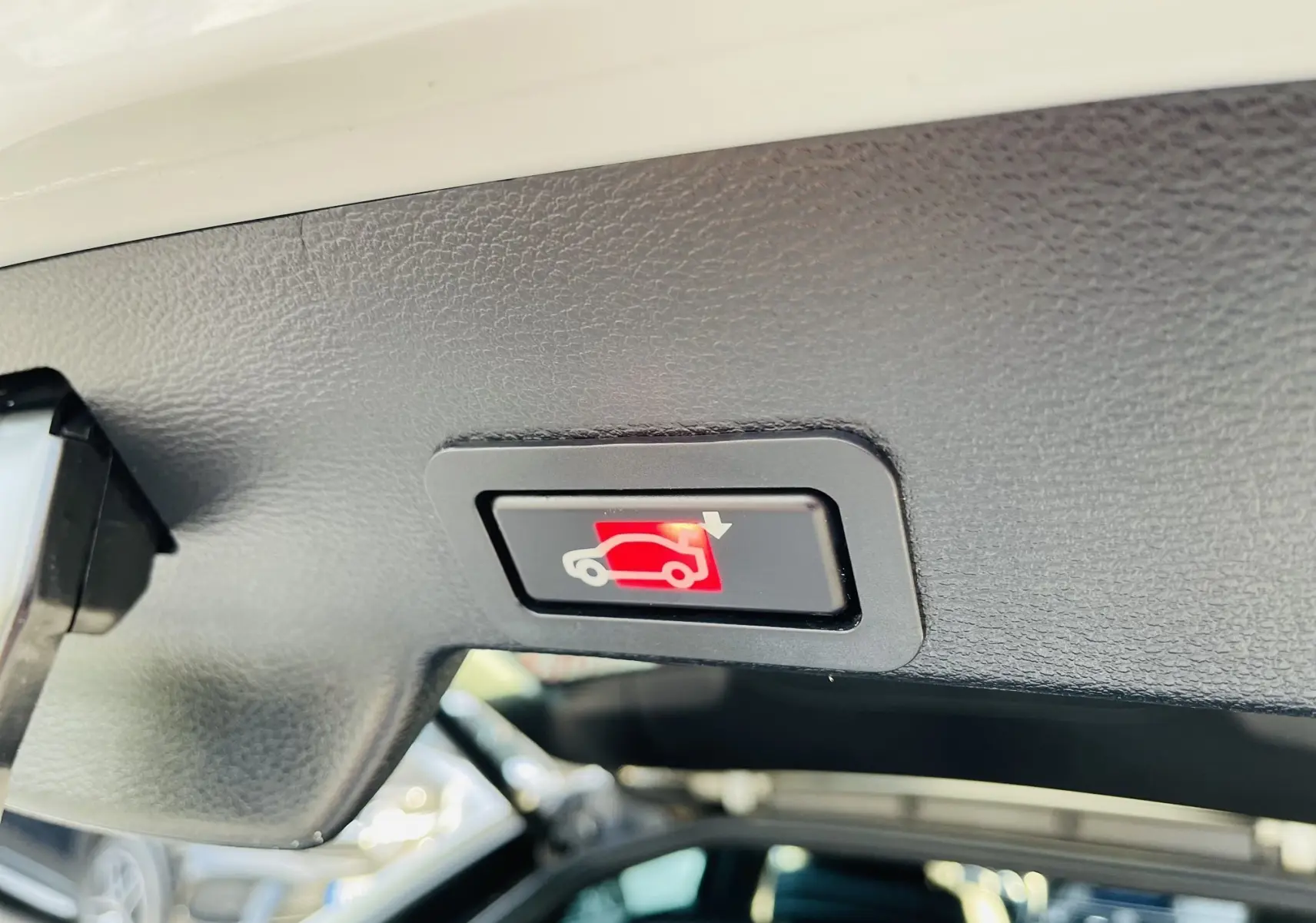 Bouton d'ouverture électrique du coffre vu de dessous dans un BMW X6 blanc, intérieur noir.