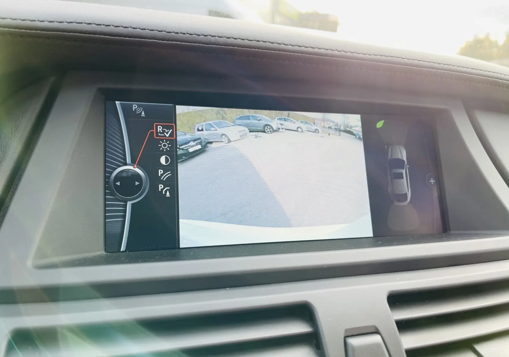 Écran intérieur du BMW X6 blanc montrant la caméra de recul avec vue Top View et commandes du système d'aide au stationnement.