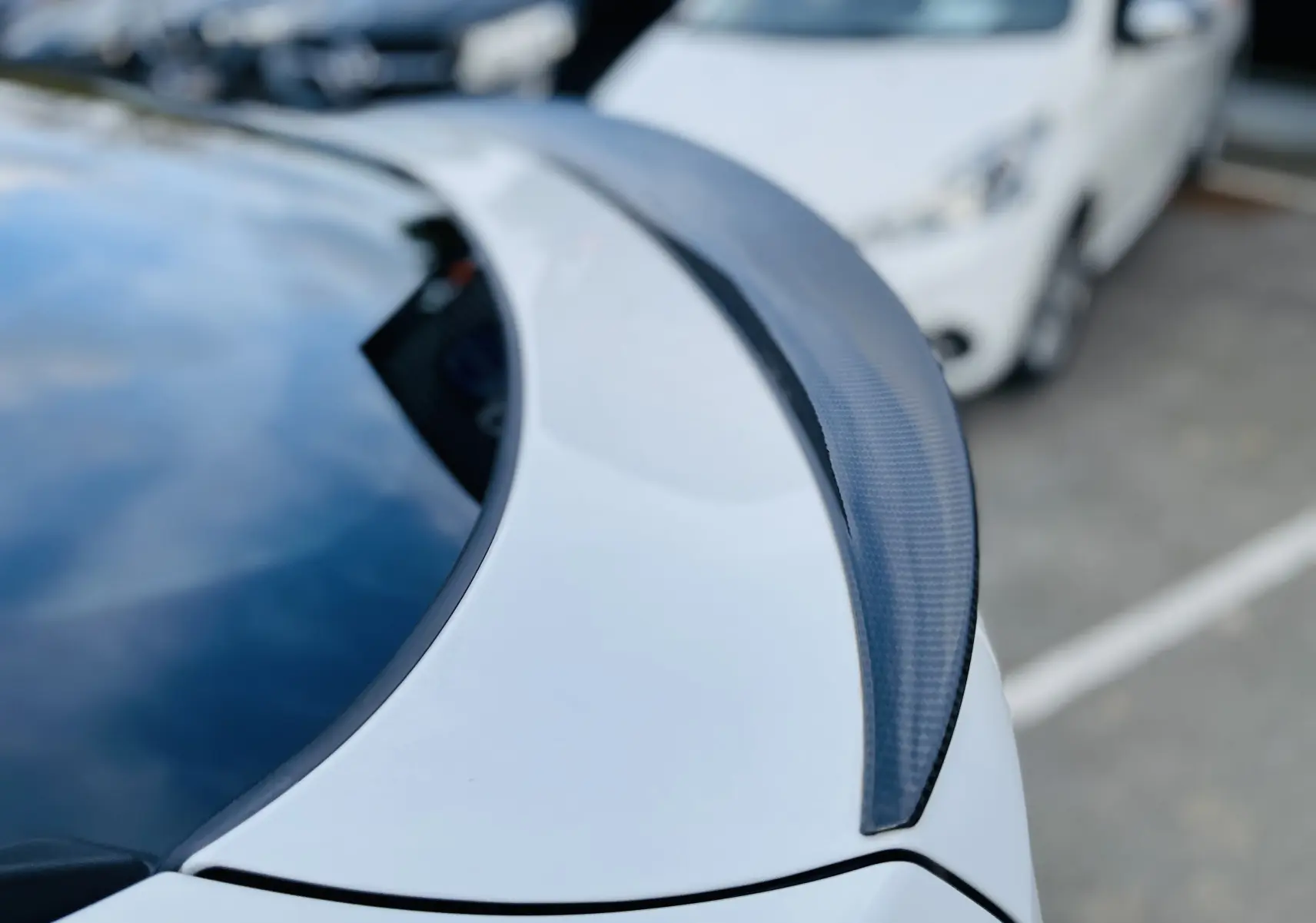 Gros plan sur l'aileron arrière en fibre de carbone du BMW X6 blanc, avec reflet du ciel sur la lunette arrière.