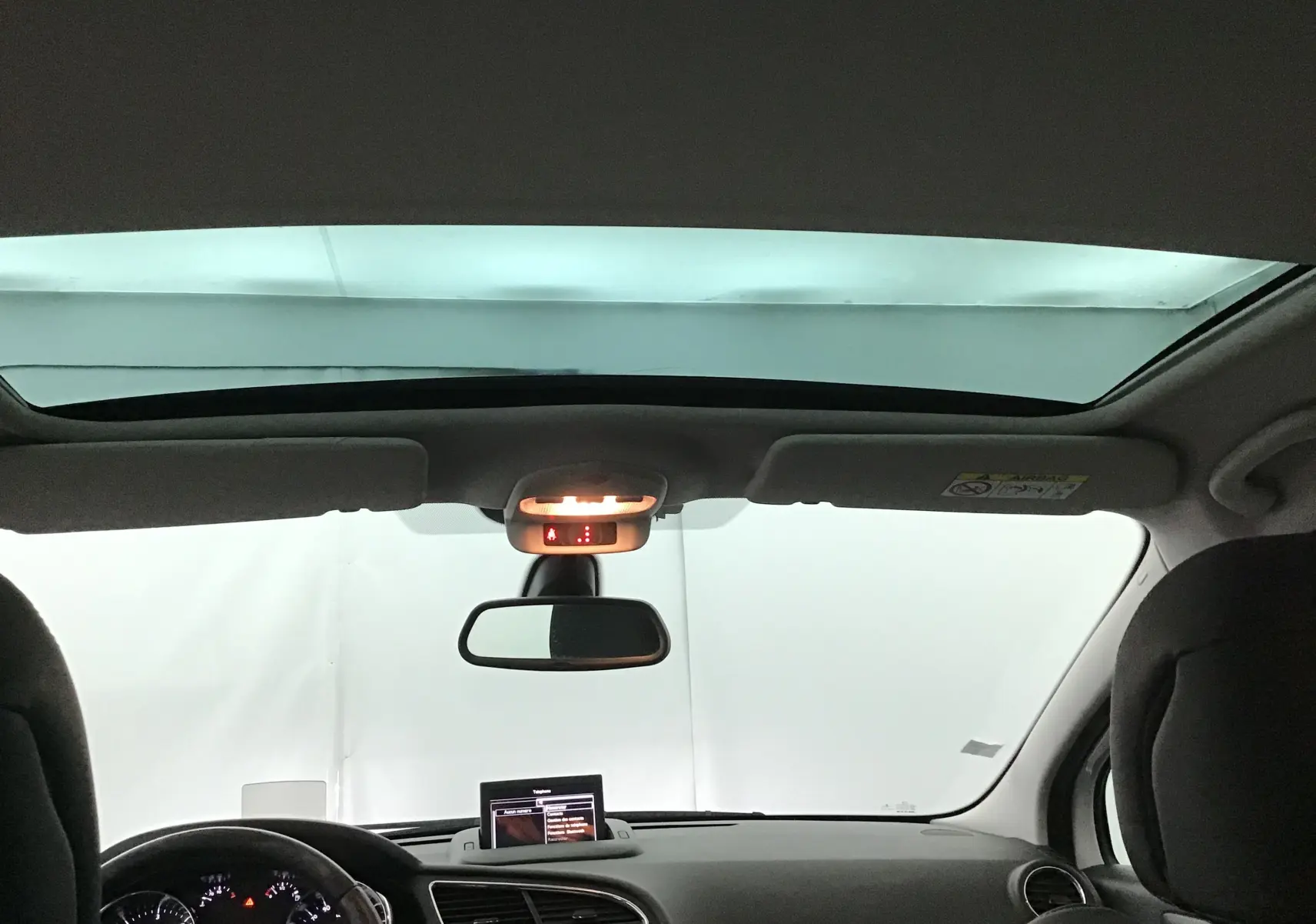Vue intérieure avant du Peugeot 3008 blanc 2015, avec toit panoramique et tableau de bord équipé d'un écran GPS.