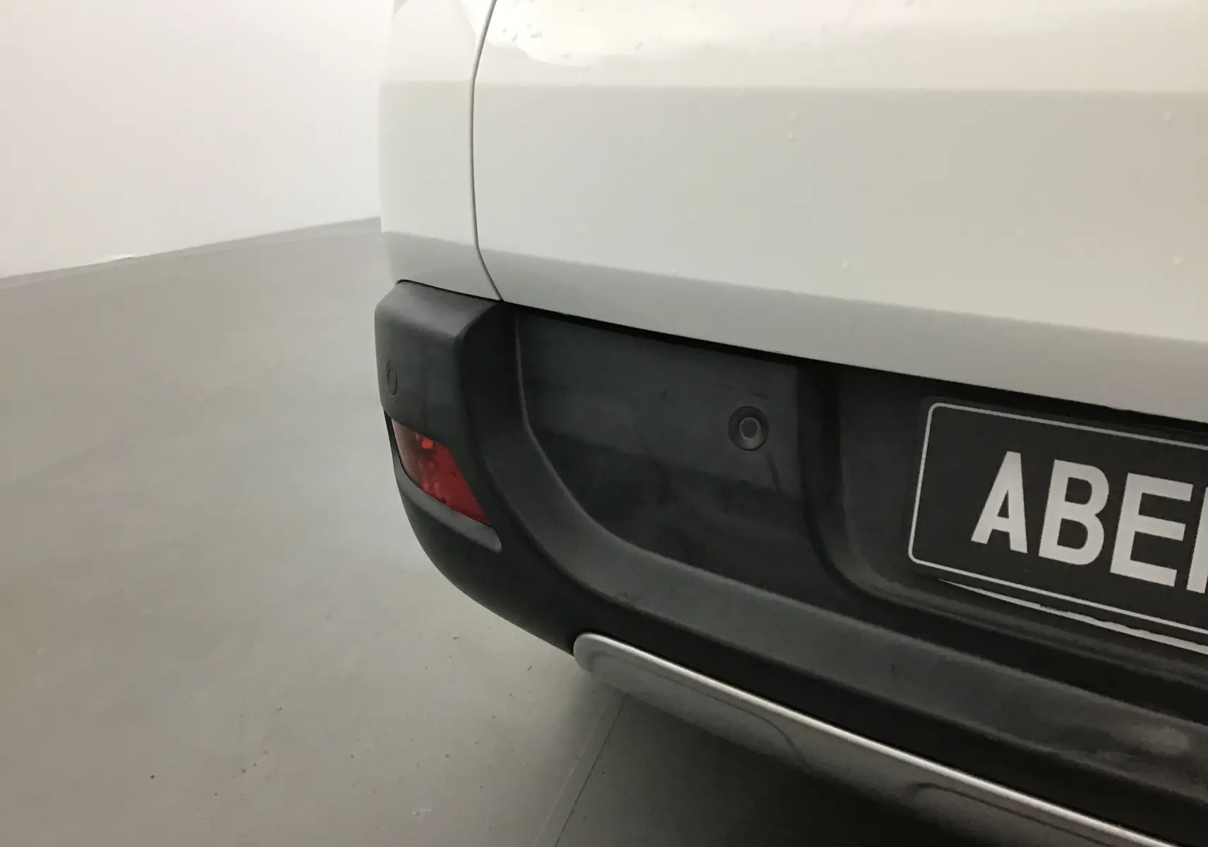 Gros plan sur le pare-chocs arrière gauche blanc du Peugeot 3008 1.6 BlueHDi 120 Allure avec radar de recul intégré.