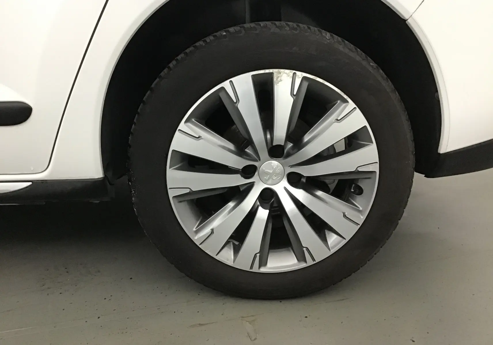 Gros plan sur la roue avant gauche d'un Peugeot 3008 blanc de 2015 avec jante alliage argentée à dix branches.