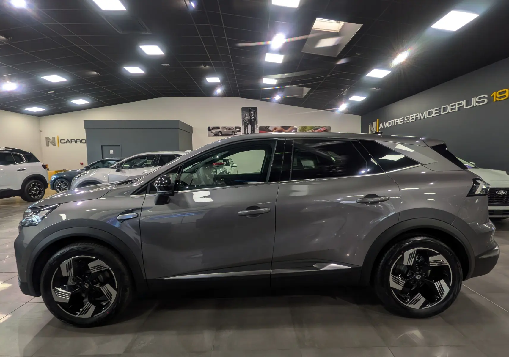 Profil côté gauche du Renault SYMBIOZ gris Cassiopé 2025 en hybride, avec jantes biton et lignes modernes dans un showroom.