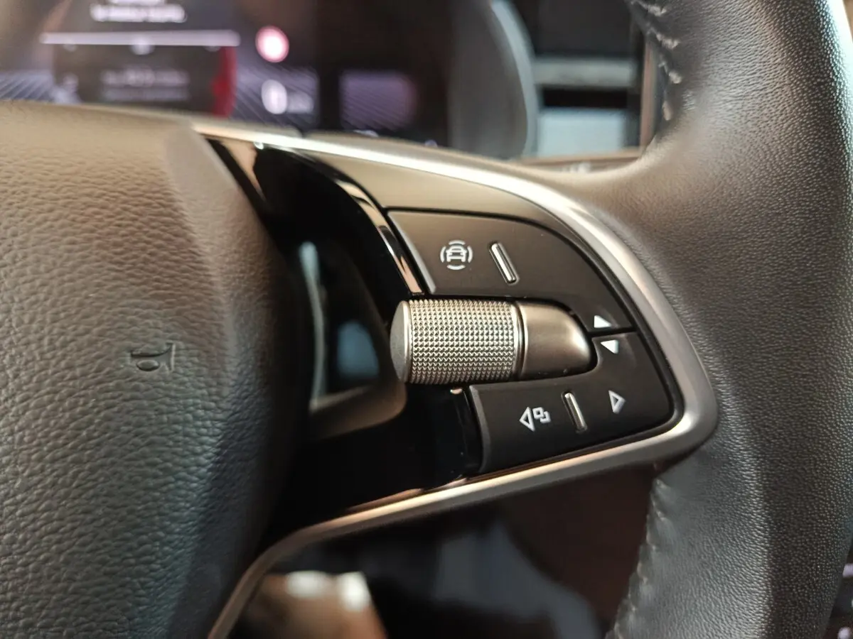 Gros plan sur le bouton multifonctions en métal du volant cuir noir du Skoda Kamiq 2024, côté gauche.