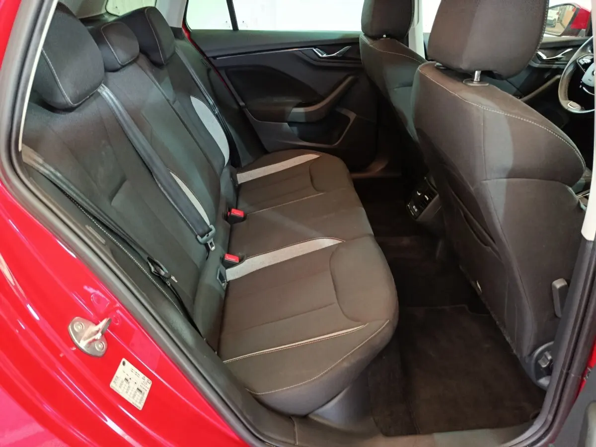 Vue intérieure côté arrière gauche du Skoda Kamiq rouge 2024, montrant la banquette tissu noire avec inserts gris.