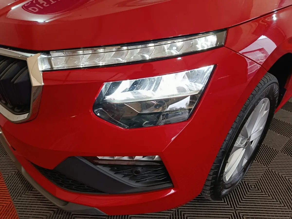 Gros plan sur l'avant droit rouge vif du Skoda Kamiq 2024, mettant en valeur le phare LED et la calandre chromée.