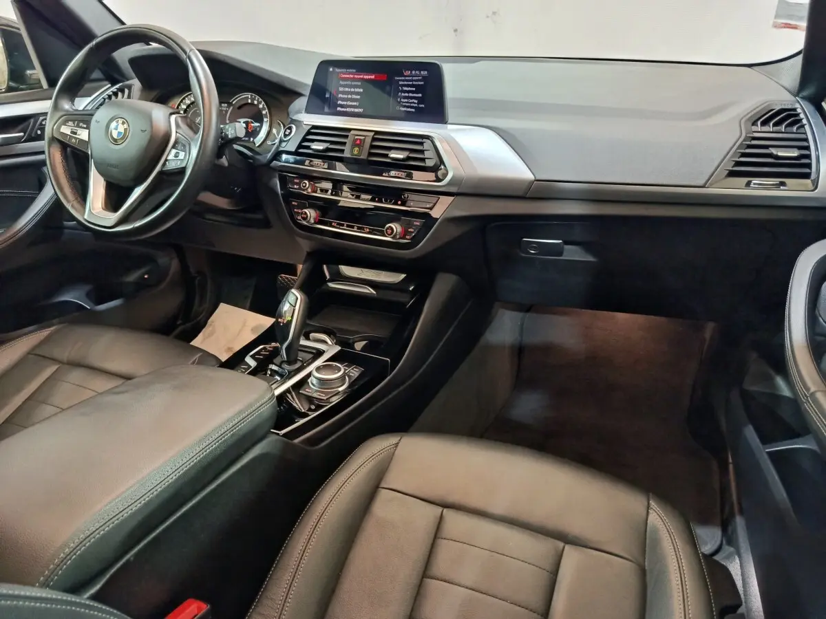 Intérieur BMW X3 xDrive30e 2020 vu côté passager, tableau de bord noir avec écran central et volant cuir multifonctions.