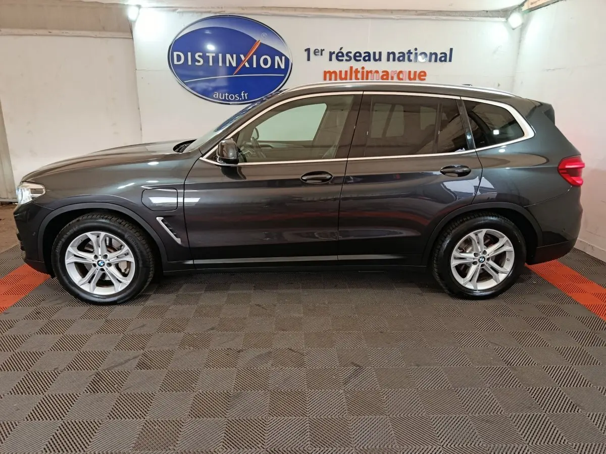 Profil droit d'un BMW X3 xDrive30e gris foncé hybride rechargeable, avec jantes alliage et prises de recharge visibles.