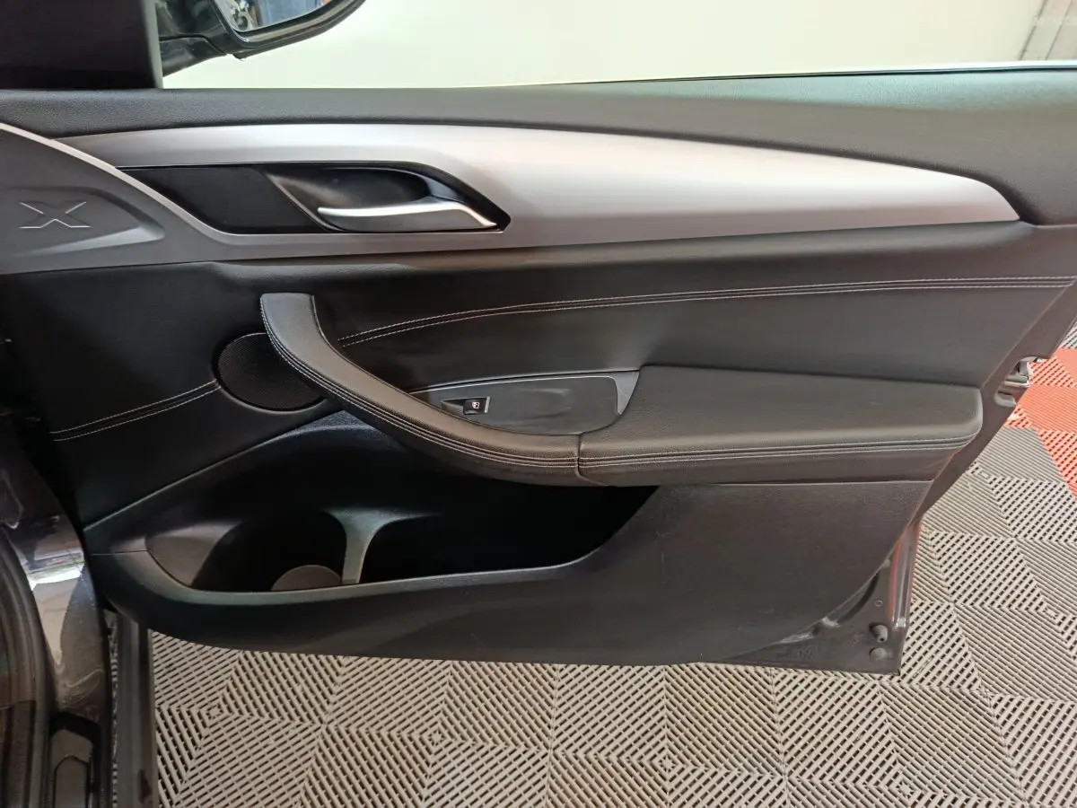 Vue latérale du panneau de porte intérieur droit noir avec poignée argentée et surpiqûres blanches du BMW X3 xDrive30e 2020.
