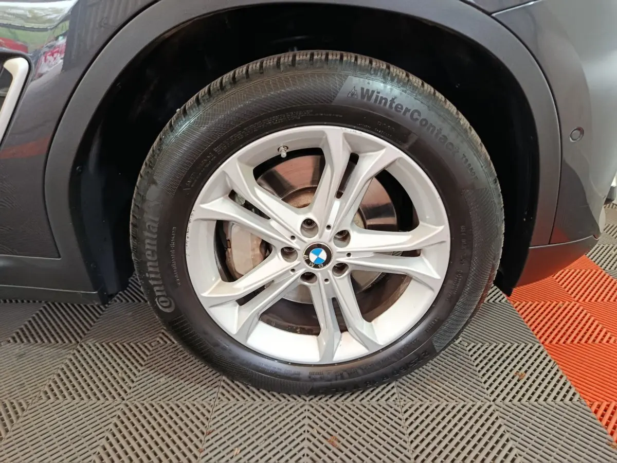 Gros plan sur la roue avant gauche d’un BMW X3 gris foncé, jante alliage argentée et pneu hiver Continental.