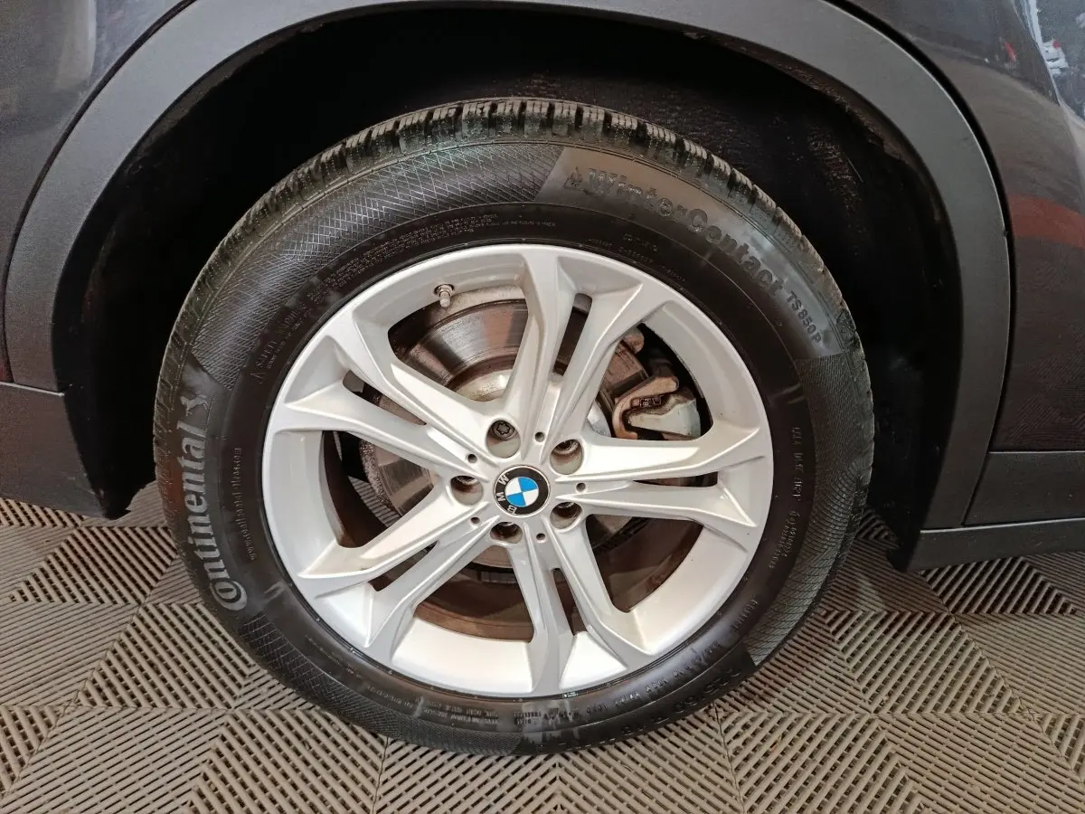Gros plan sur la roue avant droite d'un BMW X3 gris foncé, avec jante alliage argentée et logo BMW central.
