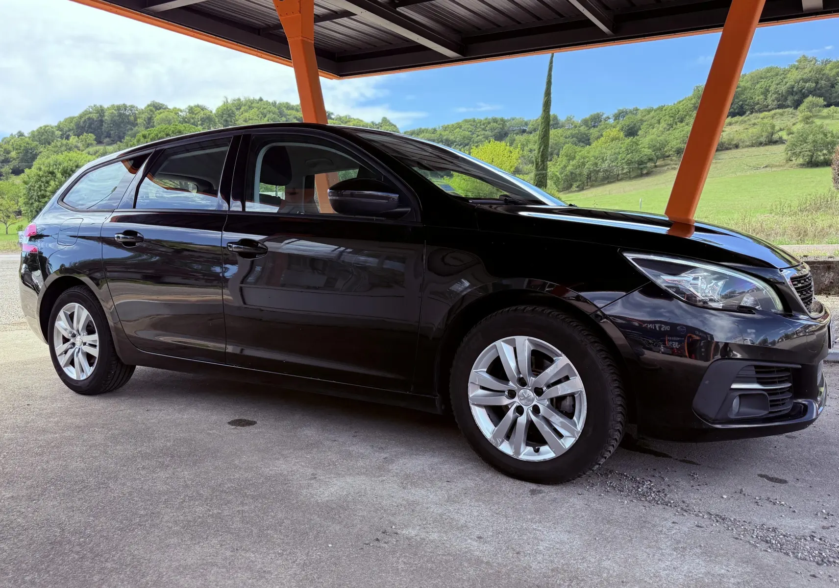 Peugeot 308 SW noir métal vue de profil côté gauche sous abri avec roues alliage et arrière allongé.