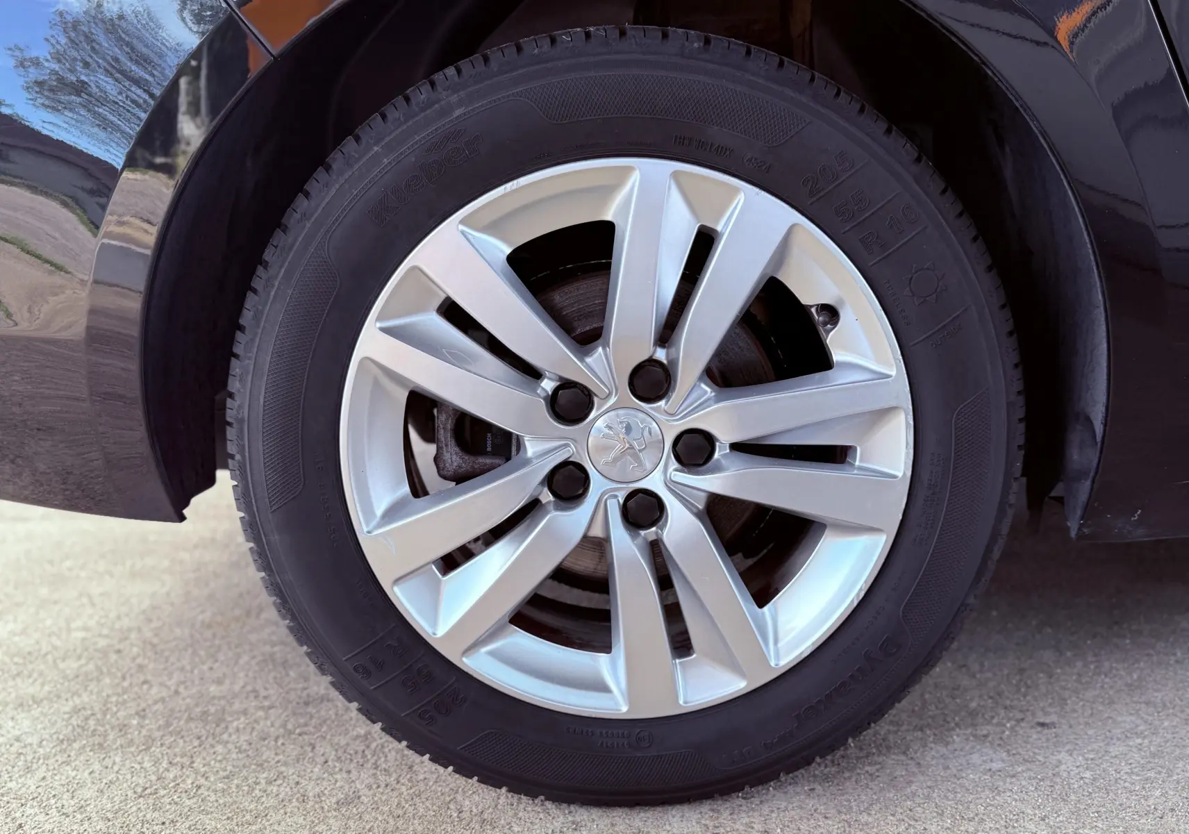 Gros plan sur la roue arrière droite de la Peugeot 308 SW noire métal, mettant en valeur la jante en alliage au design moderne.