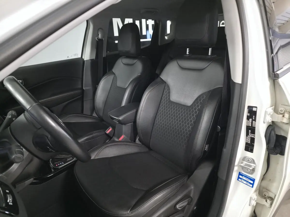 Intérieur avant du Jeep Compass blanc 2020, sièges simili cuir noirs avec motifs hexagonaux, volant visible côté gauche.