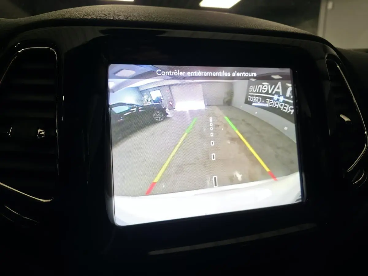 Écran central affichant la caméra de recul du Jeep Compass blanc, avec lignes de guidage colorées en parking intérieur.