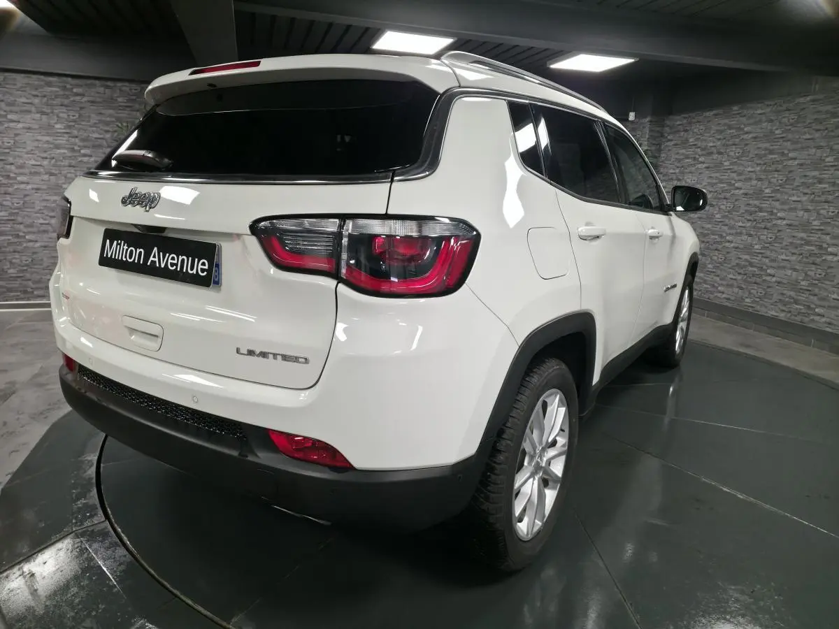 Vue 3/4 arrière droite d'un Jeep Compass blanc avec vitres surteintées et jantes alliage 18 pouces dans un showroom.