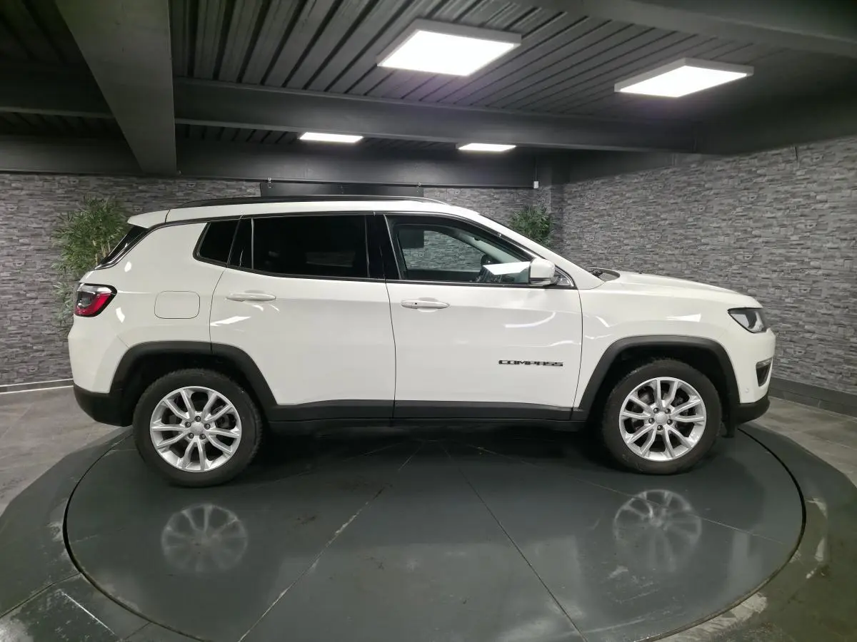Jeep Compass blanc vu de profil côté gauche avec jantes alliage 18 pouces et vitres surteintées dans un studio.