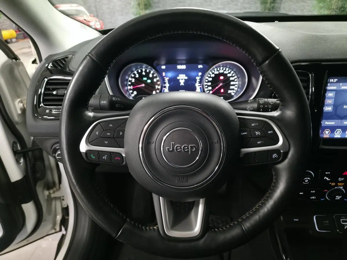 Vue rapprochée du volant en cuir noir du Jeep Compass 2020 avec tableau de bord et écran tactile visibles.