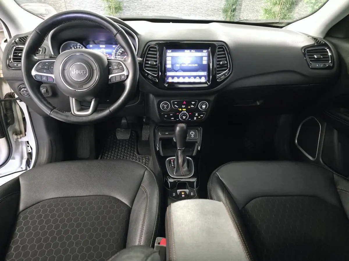 Vue intérieure avant du Jeep Compass 2020 avec volant cuir, écran tactile central et sièges simili cuir noirs.