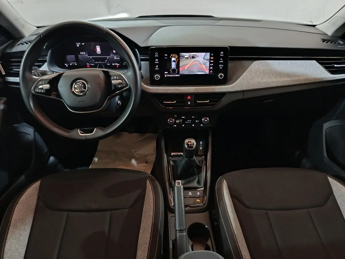 Vue intérieure frontale du tableau de bord et volant cuir noir du Skoda Kamiq 2024 avec écran tactile central et boîte manuelle.
