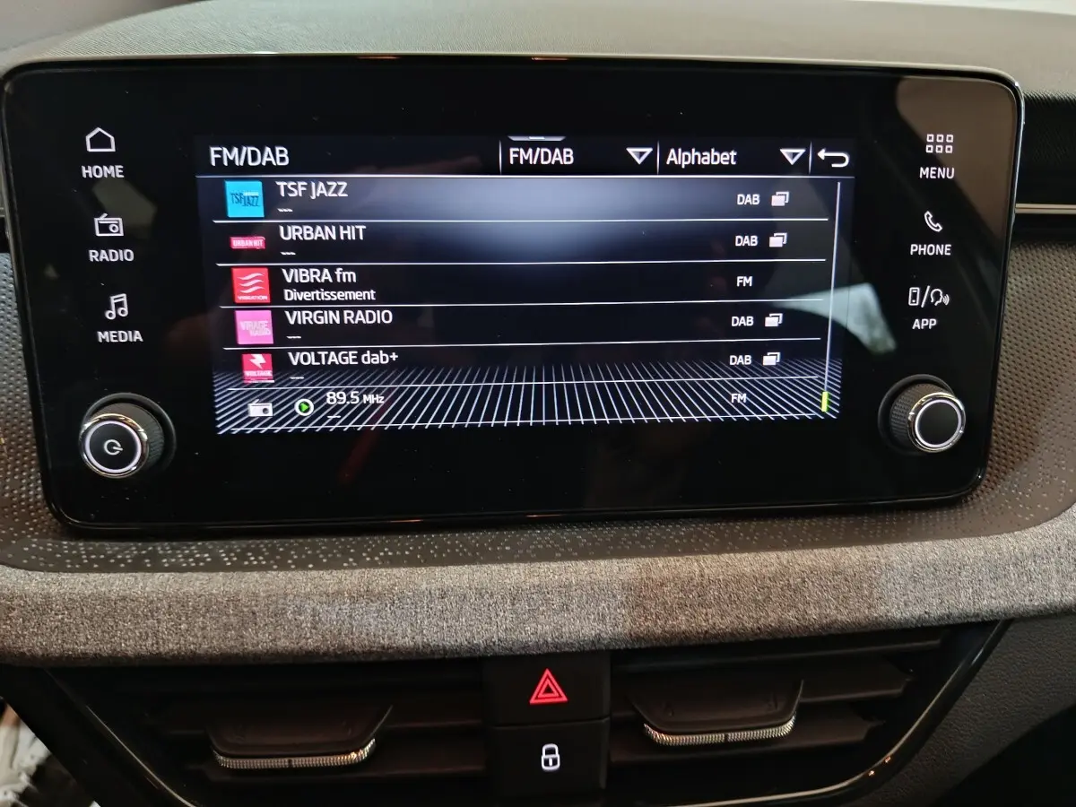 Écran tactile central du Skoda Kamiq 2024 affichant les stations radio FM/DAB, entouré de commandes noires.
