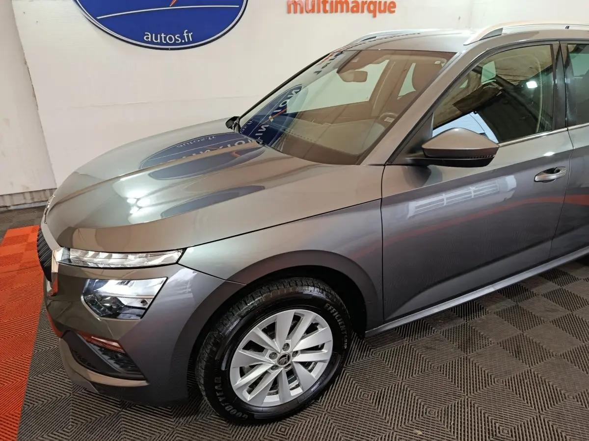 Vue 3/4 avant droit d'un Skoda Kamiq gris clair avec phares LED et jantes alliage en intérieur showroom.